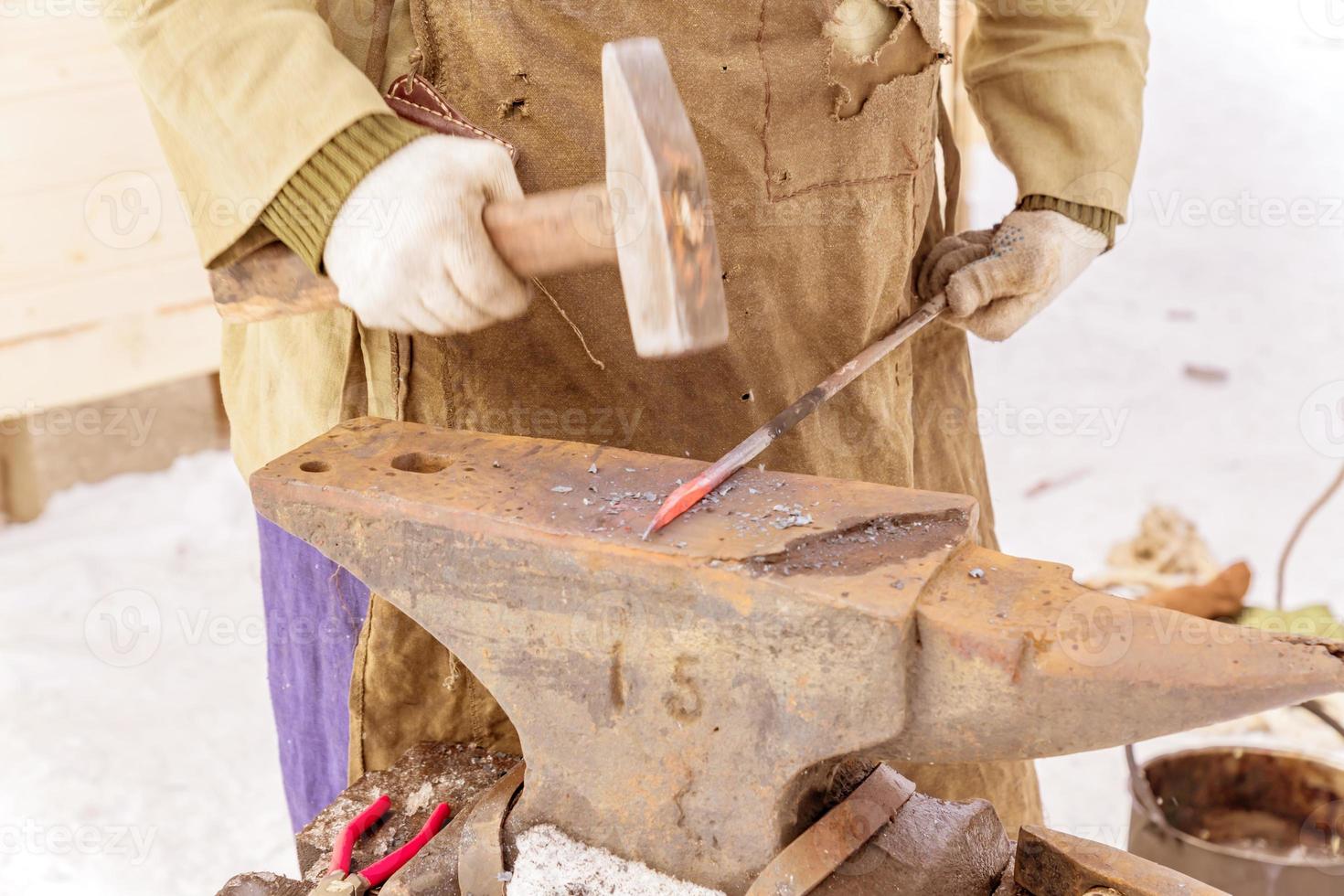 blacksmith manually forging the molten metal on the anvil outdoors photo