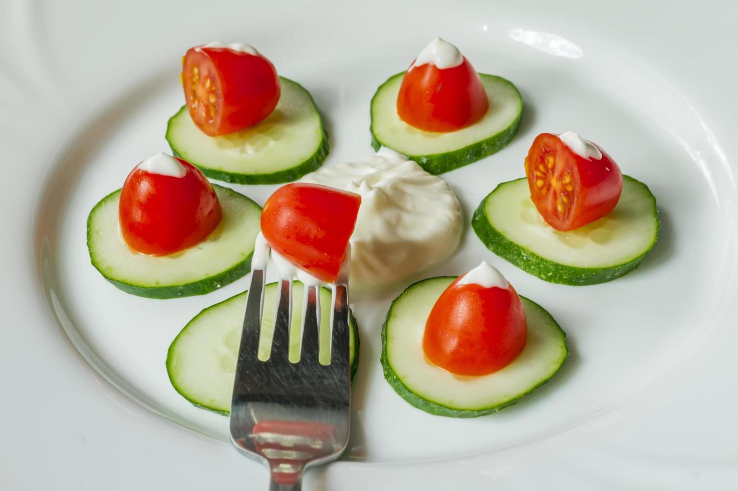 Cherry tomatoes an sliced cucumbers with mayoneese sauce on a plate. Fresh salad photo
