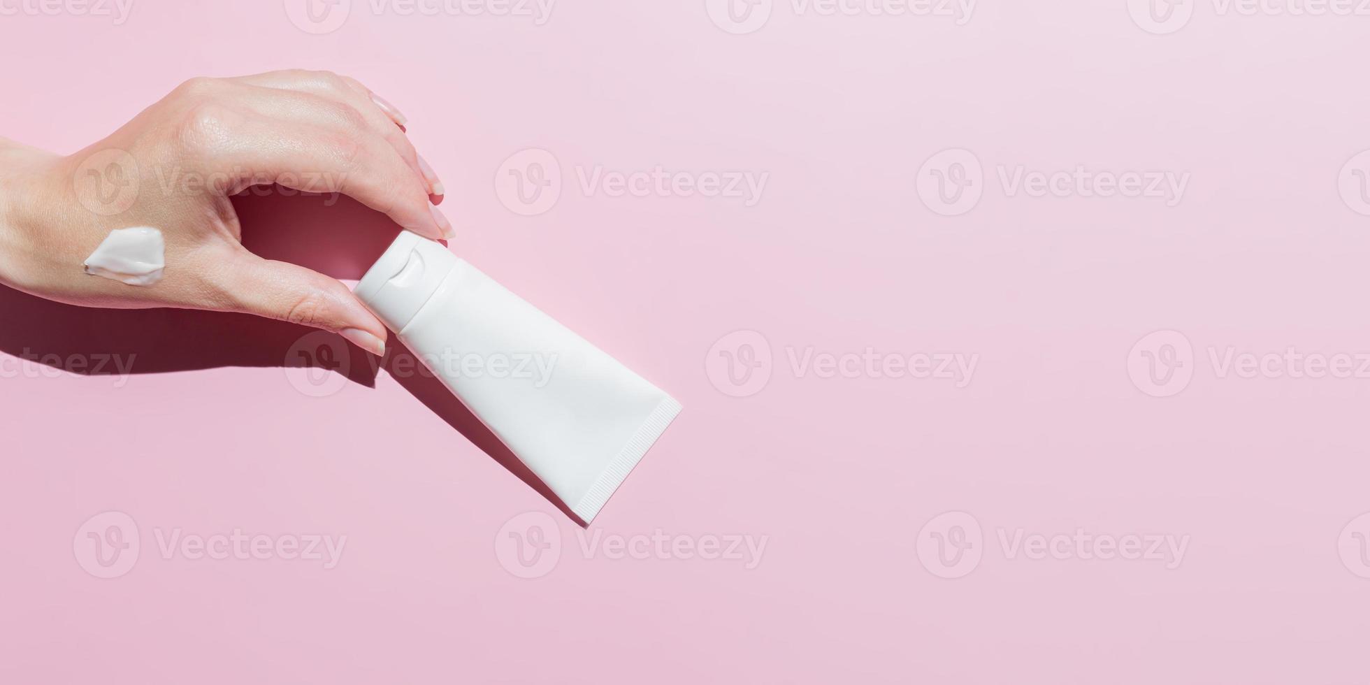 Women's hands holding tube of cream on a pink background. Mock up moisturizing hand cream. Banner. Cream swatch photo