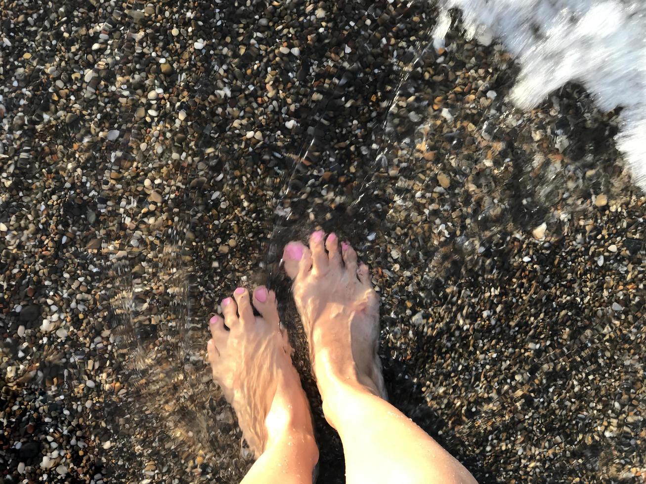 un par de pies de mujer en el fondo de la playa de guijarros foto