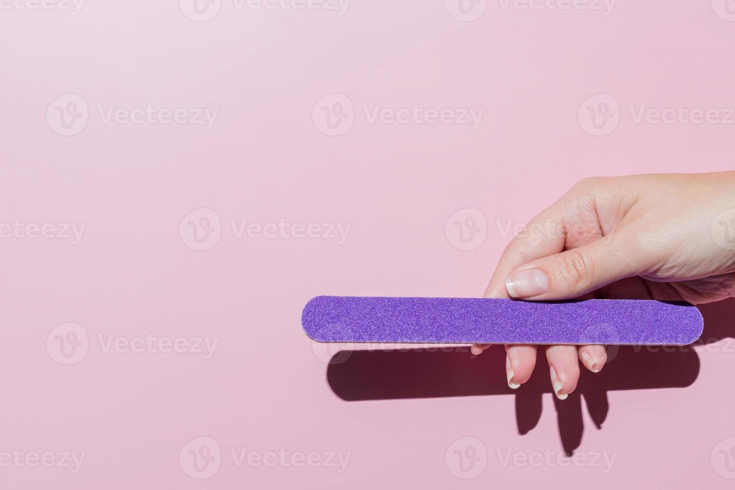 female hand filing nails polish on pink background. Concept of lady painting, polishing nails. Nail brush, nail polish, nail file. Spa treatment beauty. Flat lay with copy space photo