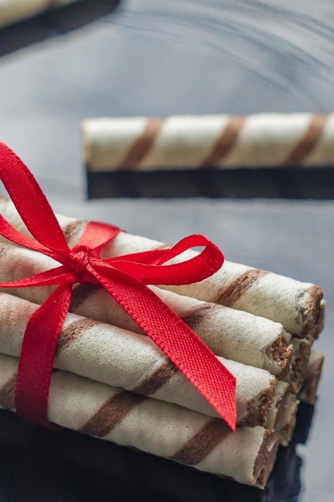 rollos de oblea con chocolate y cinta roja sobre fondo negro foto