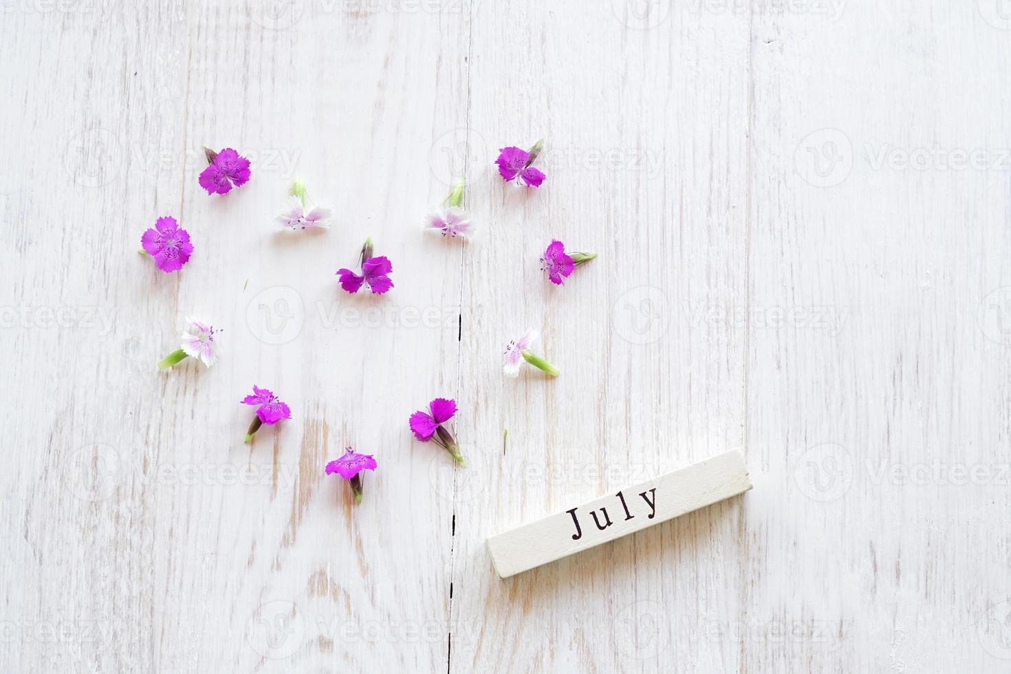 top view of wooden calendar with July sighn and pink flowers. photo