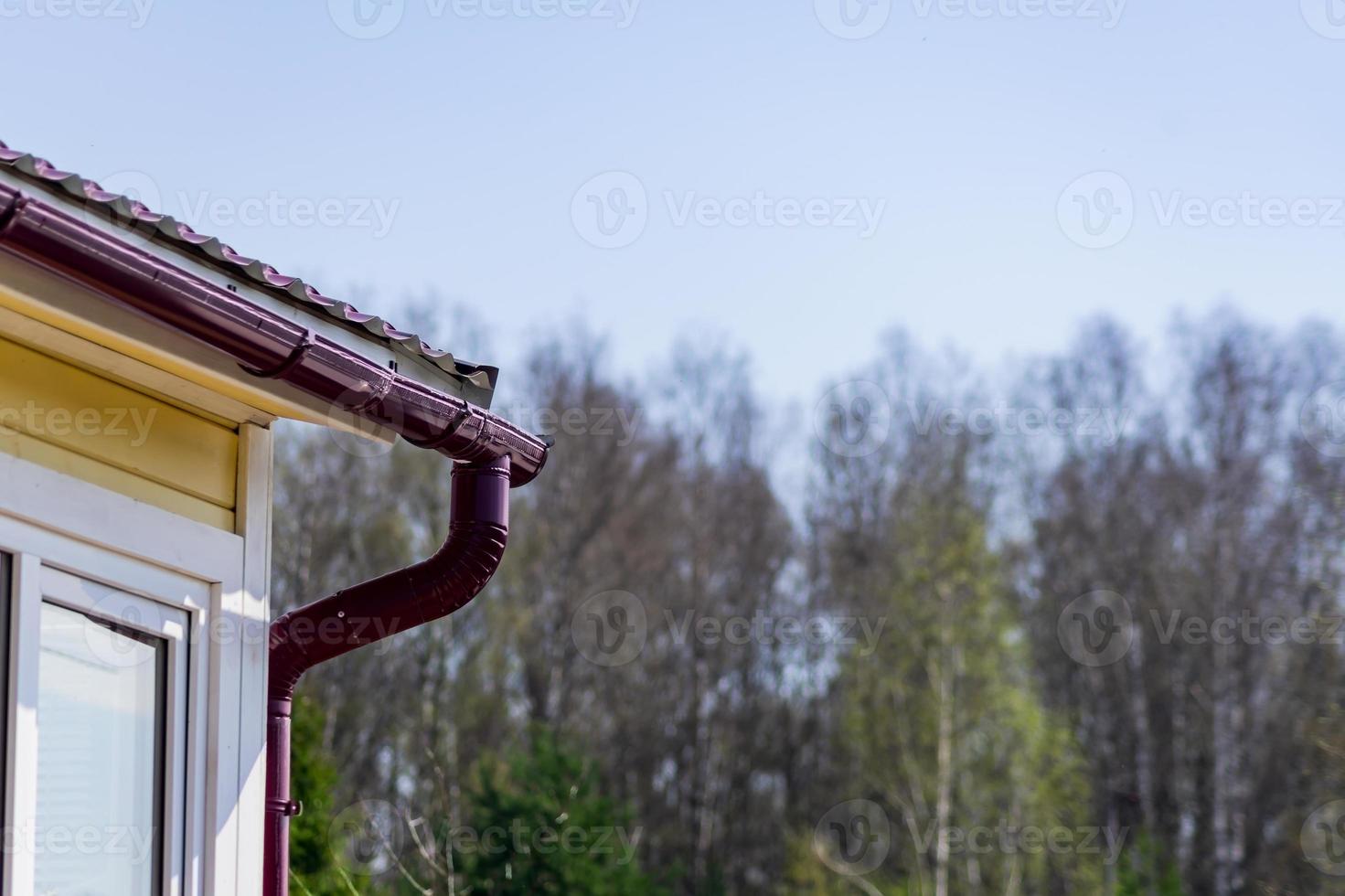 Corner of the house with gutter on a background of blue sky and forest photo