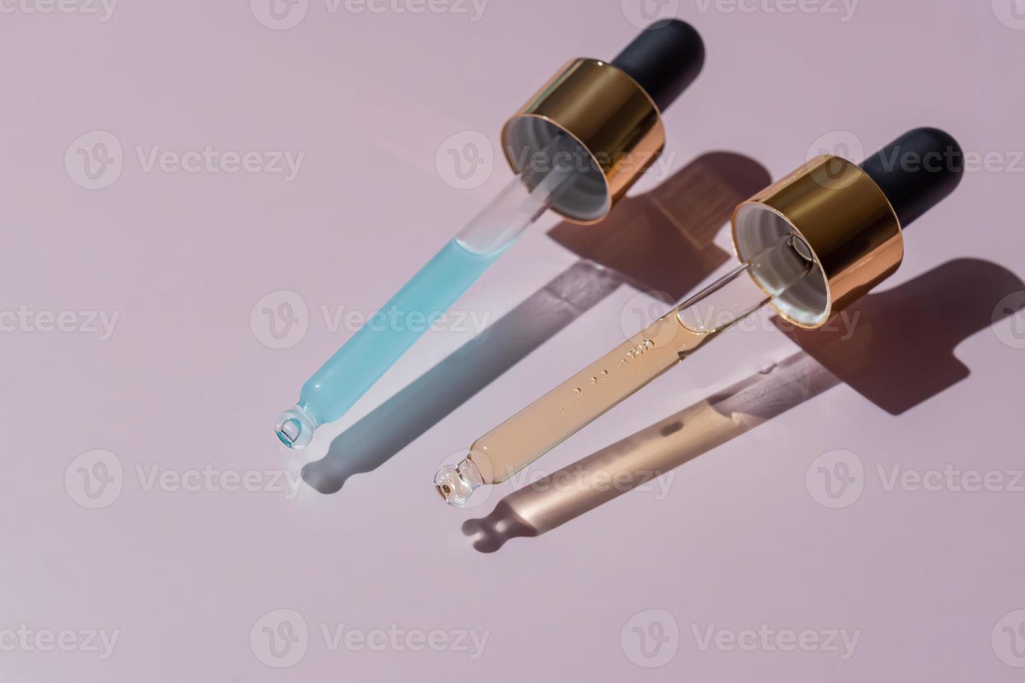Close up of pipettes with pouring liquid essential oil or serom on pink background. Dropper with a falling drop of aromatherapy oil close-up photo