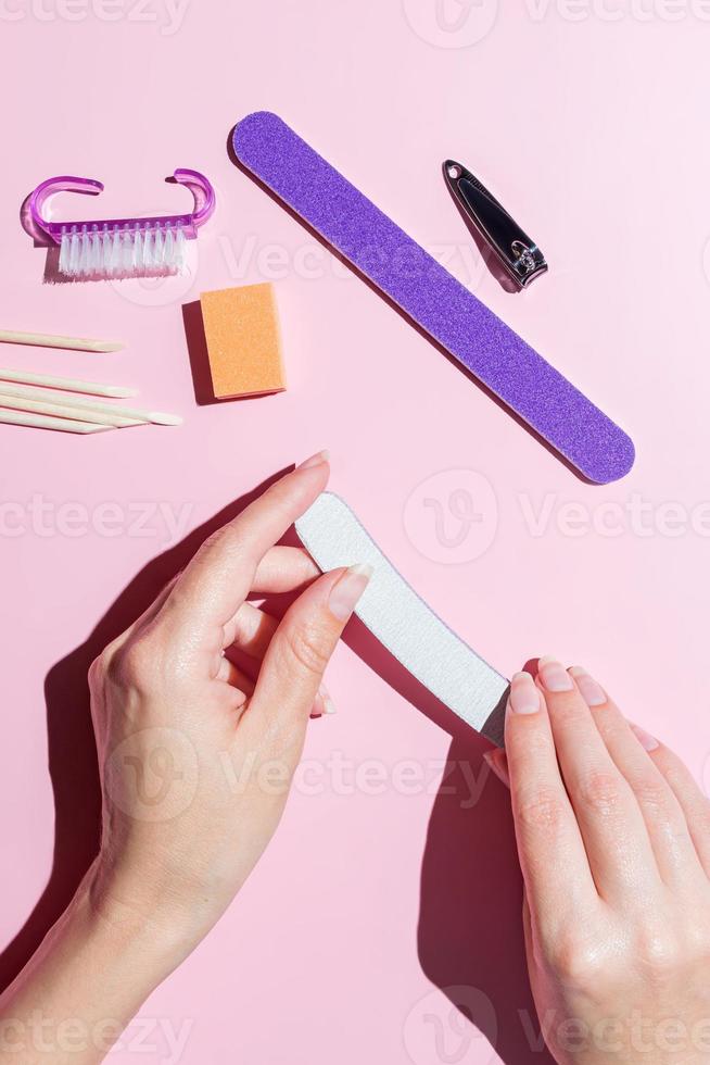 A woman makes herself a manicure, takes care of her nails and fingers at the table at home. Sharpen nails align with a file, top view close-up photo