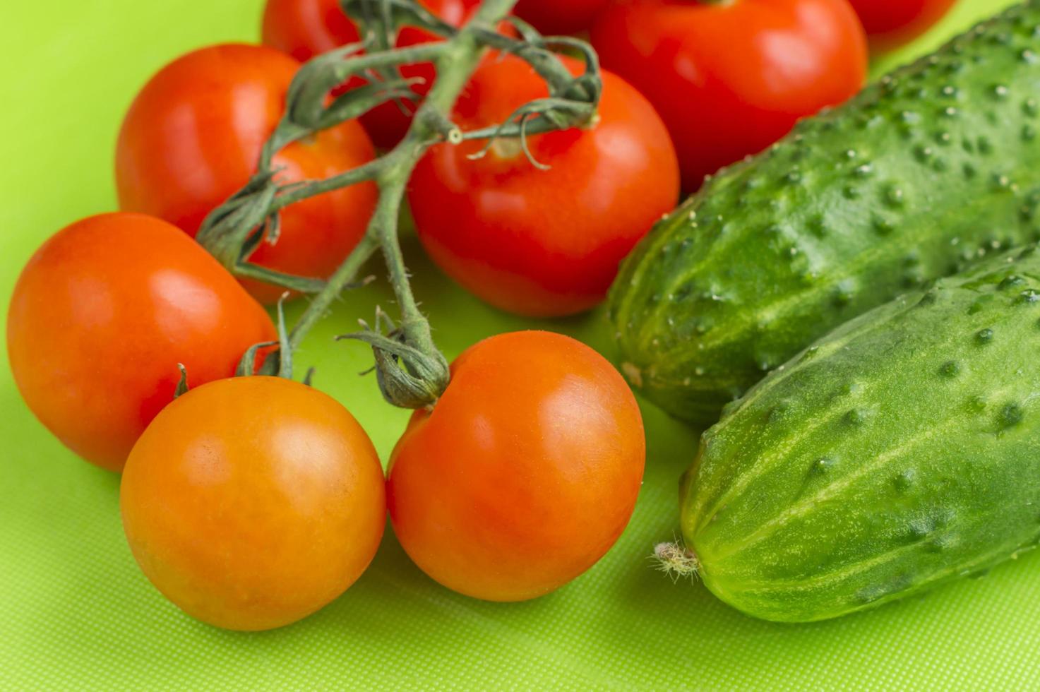 Red cherry tomatoes and green cucumbers on green cutting board photo