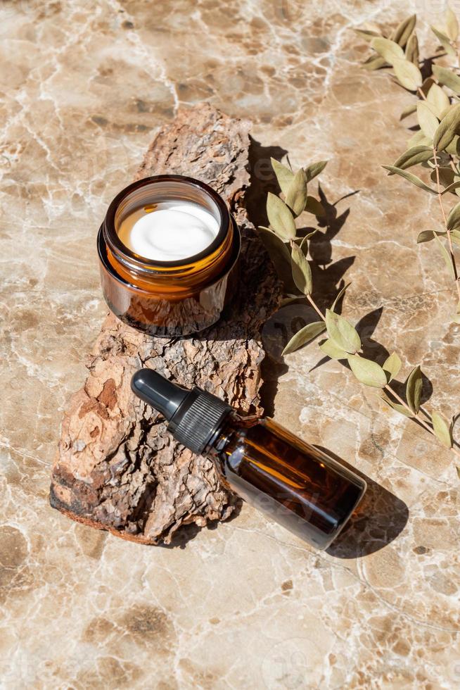 tarro de crema hidratante, suero en botella de vidrio sobre corteza de árbol. set para productos de belleza para el cuidado de la piel y el cuerpo. paquete sin marca con etiquetas en blanco foto