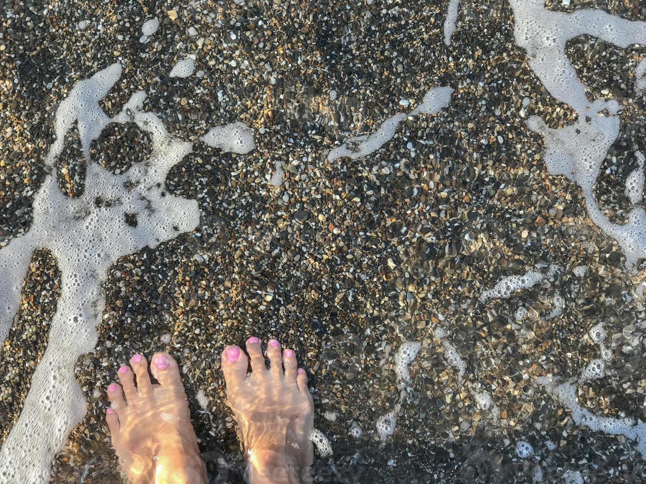 un par de pies de mujer en el fondo de la playa de guijarros foto