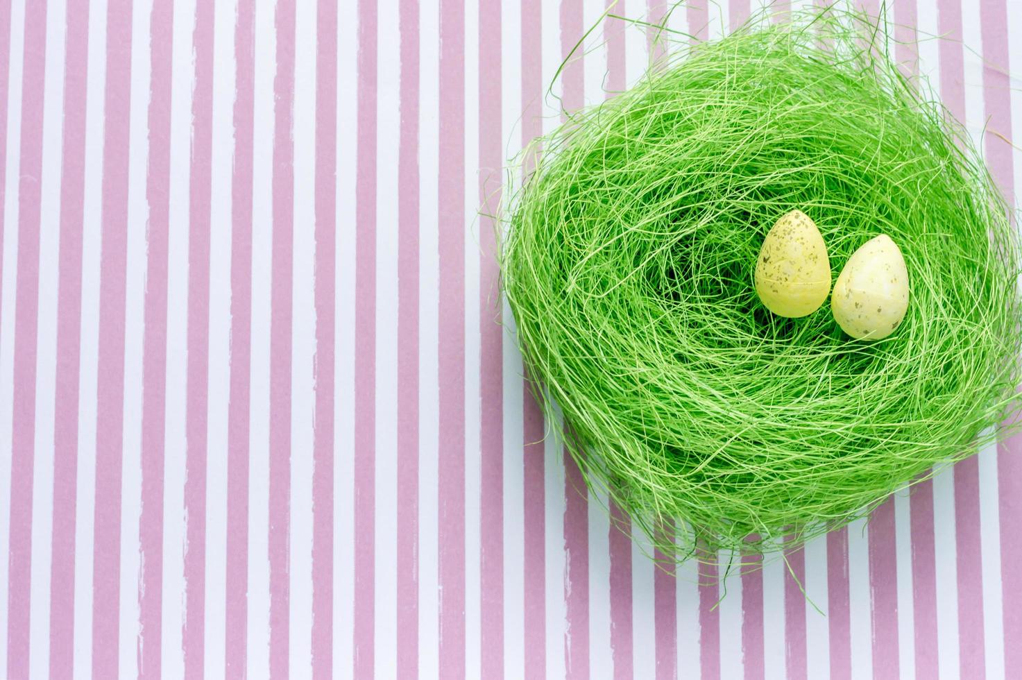 Artificial green nest with two eggs on striped background photo