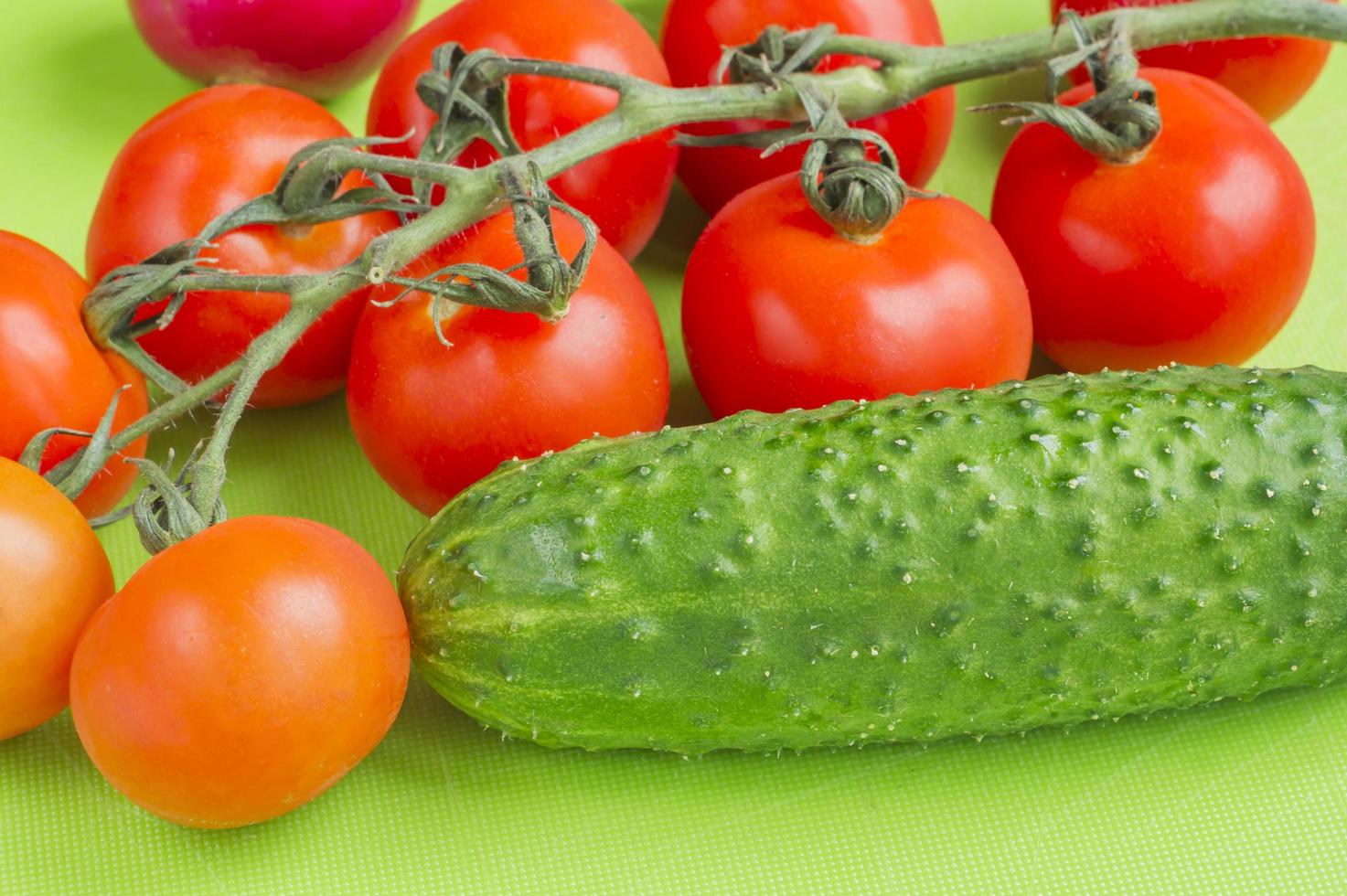 Red cherry tomatoes and green cucumbers on green cutting board photo