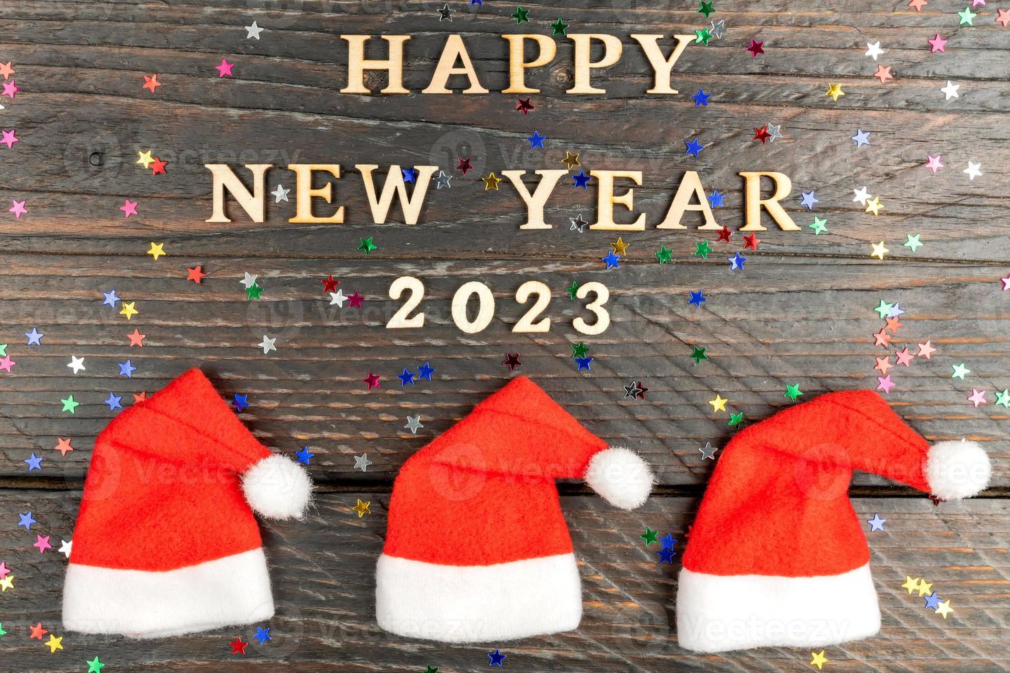 festive greeting card for 2023 new year with red santa hats in a row and wooden text on a table. photo