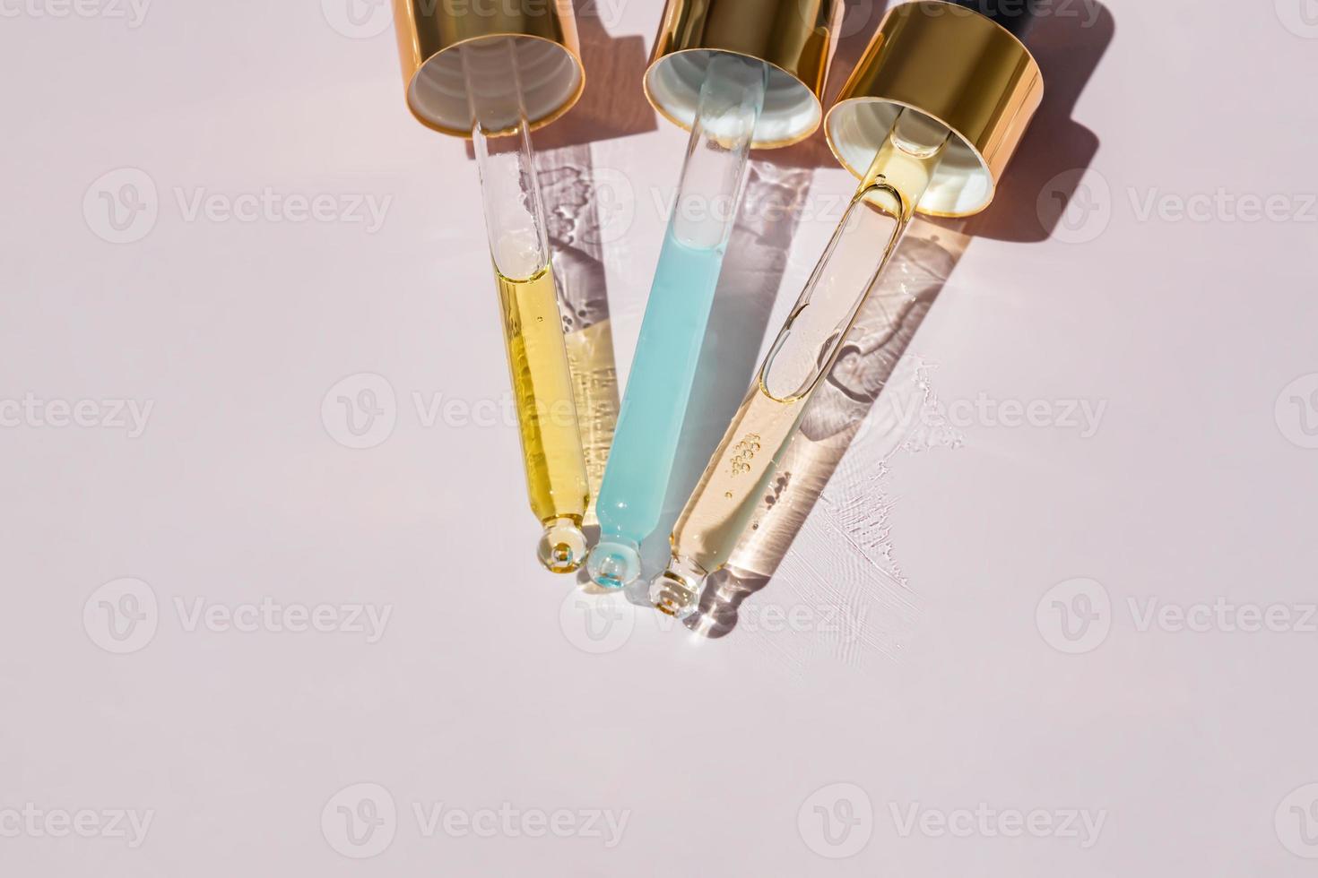 Close up of pipettes with pouring liquid essential oil or serom on pink background. Dropper with a falling drop of aromatherapy oil close-up photo