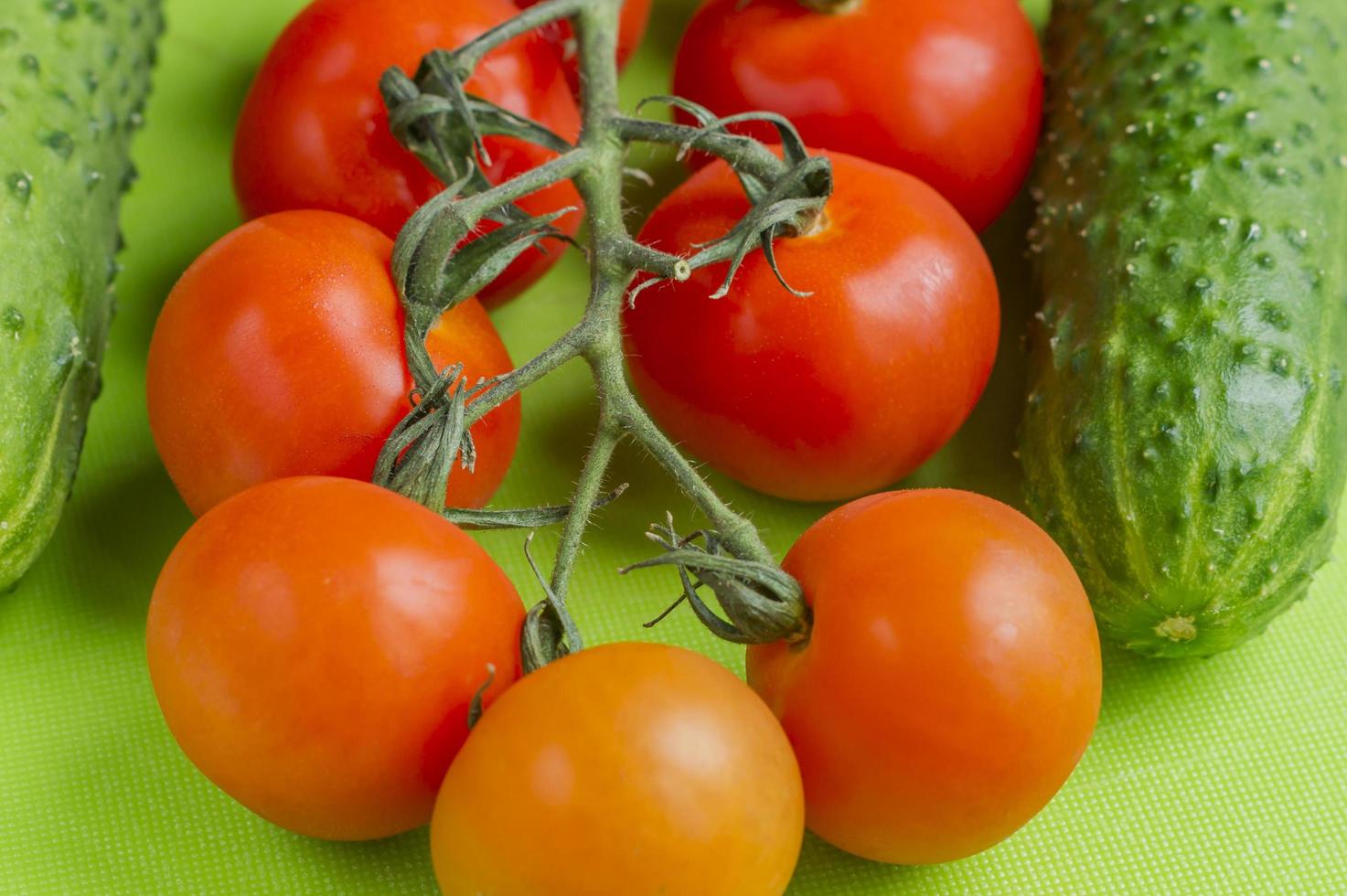 Red cherry tomatoes and green cucumberson green cutting board photo