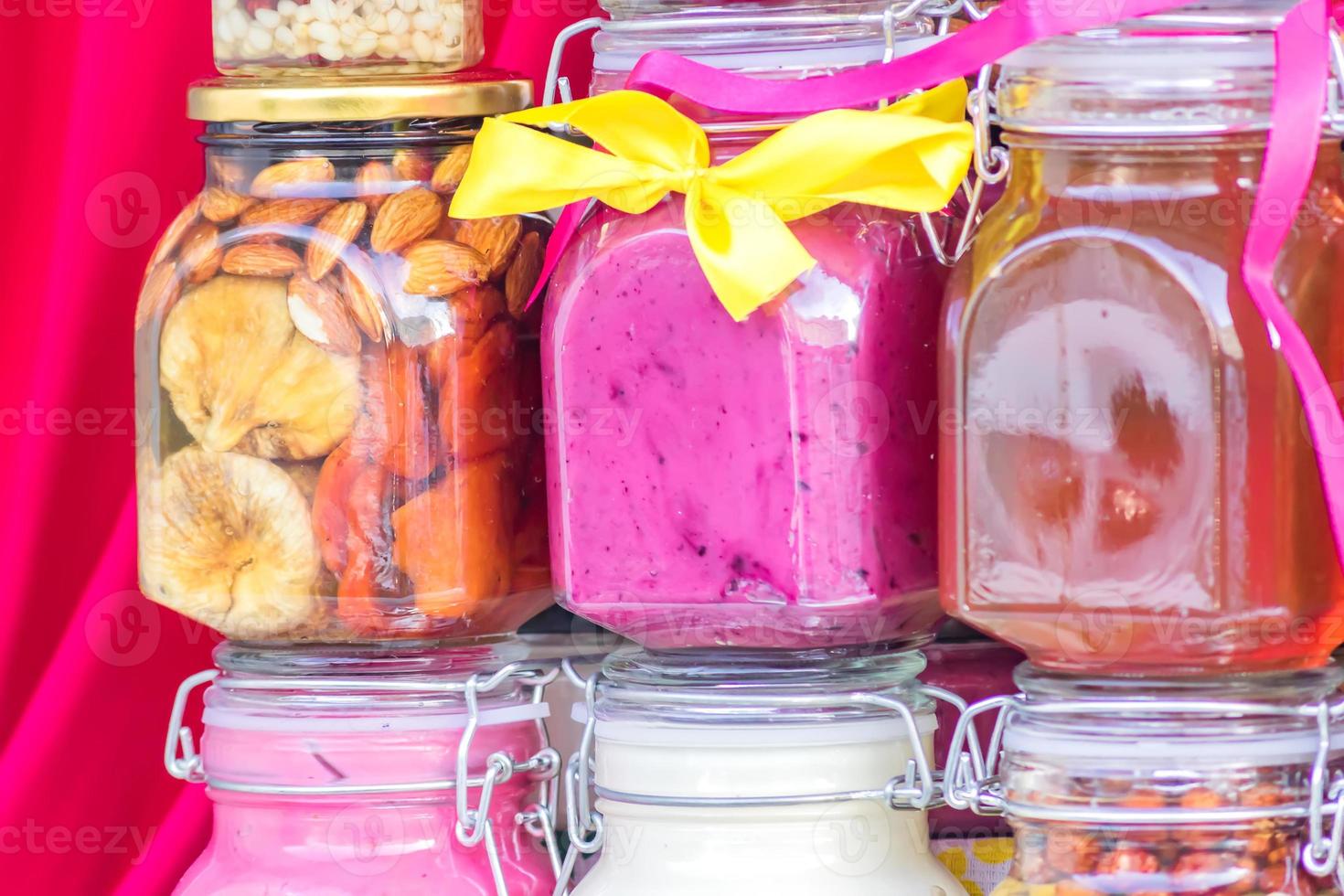 Glass jars with different sorts of honey on red background photo