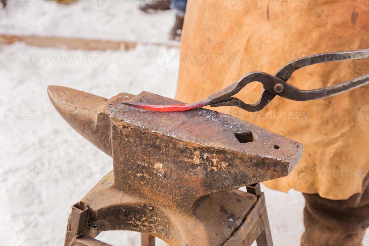 blacksmith manually forging the molten metal on the anvil outdoors photo