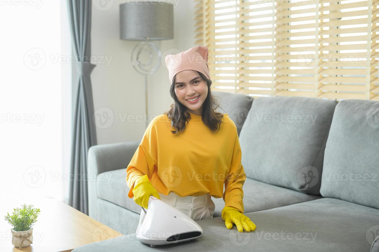 joven mujer feliz usando guantes amarillos y aspirando un sofá en la sala de estar. foto