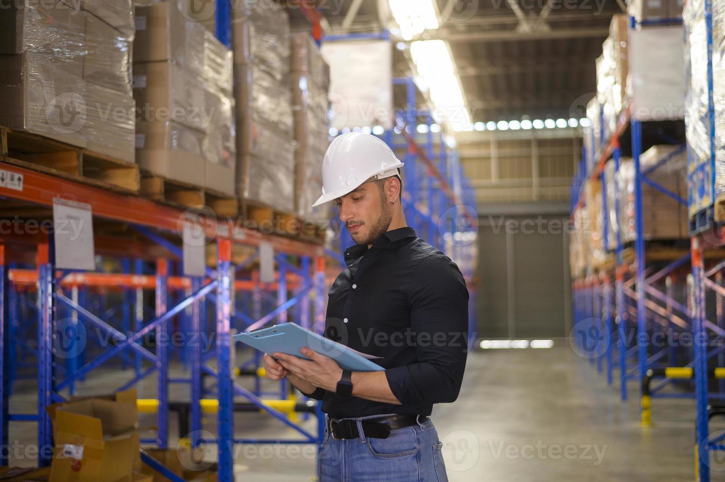 Young worker wearing helmet checking inventory and counting product on shelf in modern warehouse. photo