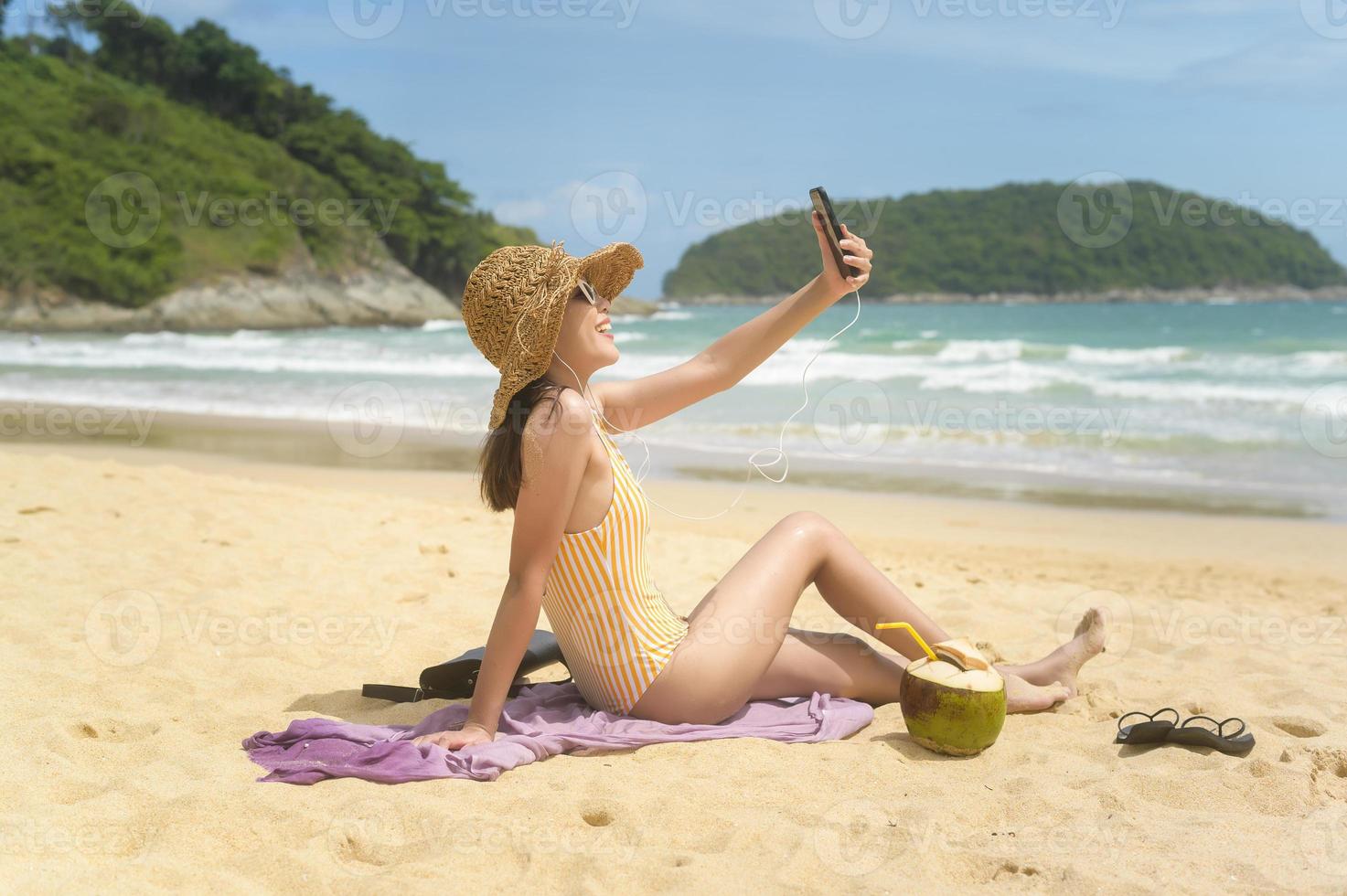Young Beautiful woman in Bikini listening to music and using smartphone on the beach,  Summer, vacation, holidays, Lifestyles concept. photo