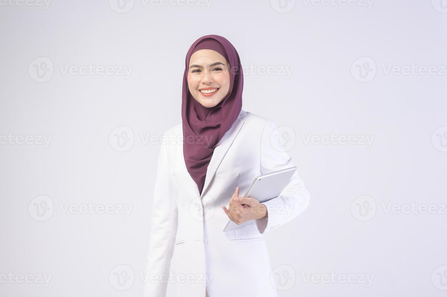 Beautiful muslim business woman wearing white suit with hijab holding tablet in studio photo