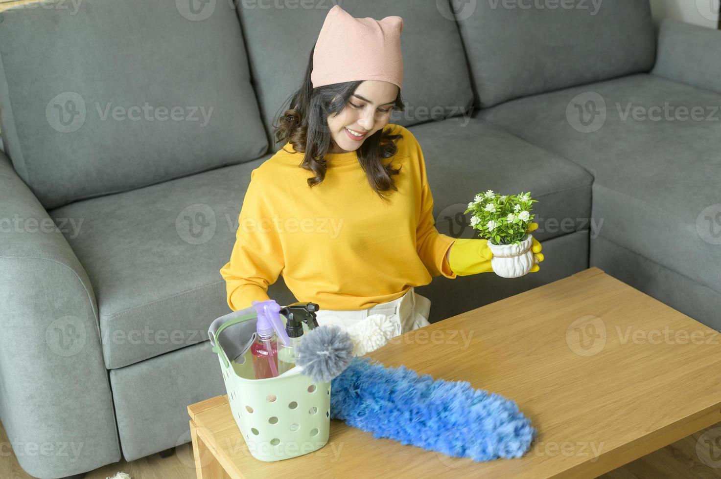 Young happy woman wearing yellow gloves  and dusting the table in living room. photo