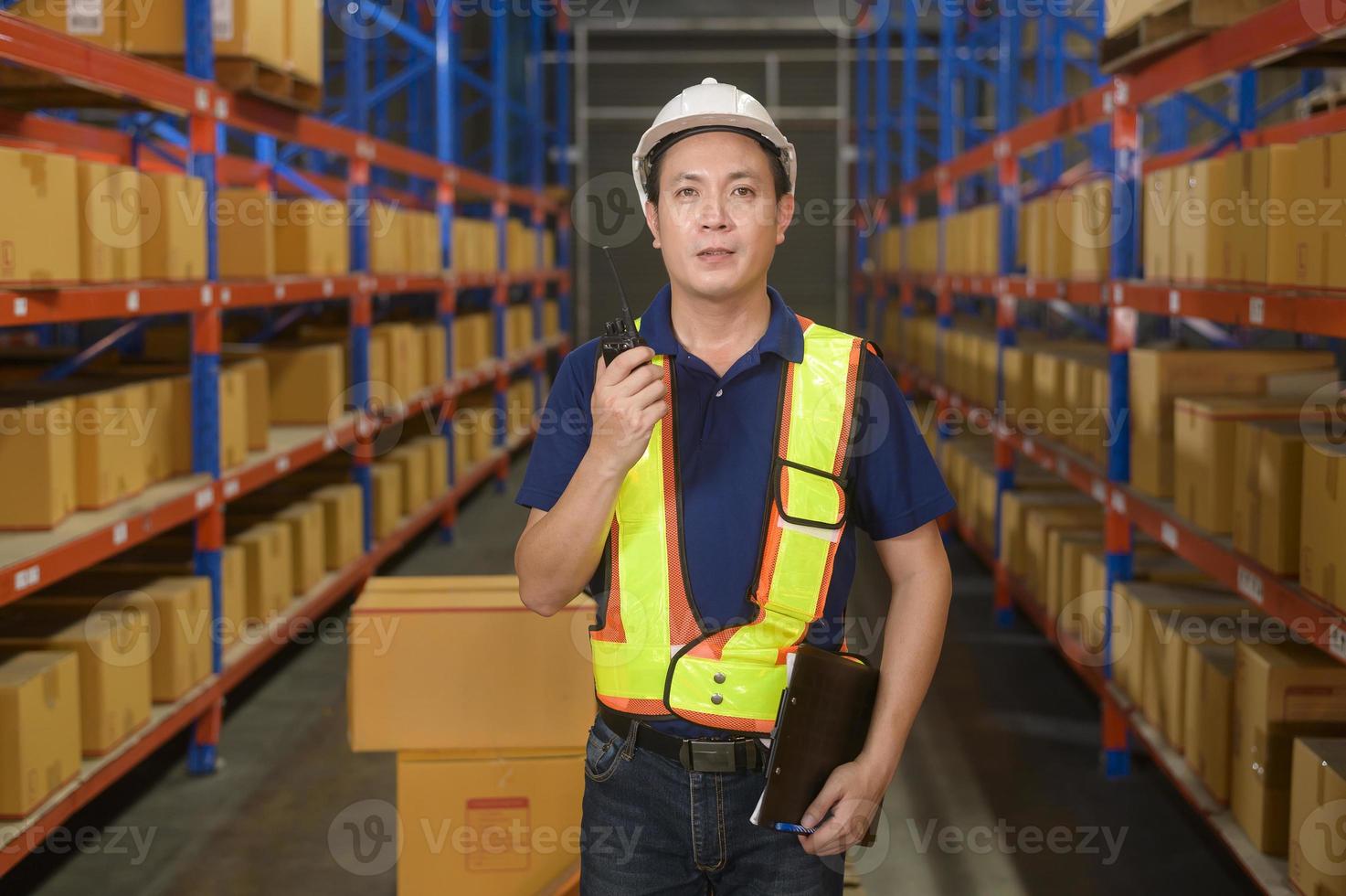 Young asian male worker wearing helmet using talki walki in modern warehouse. photo