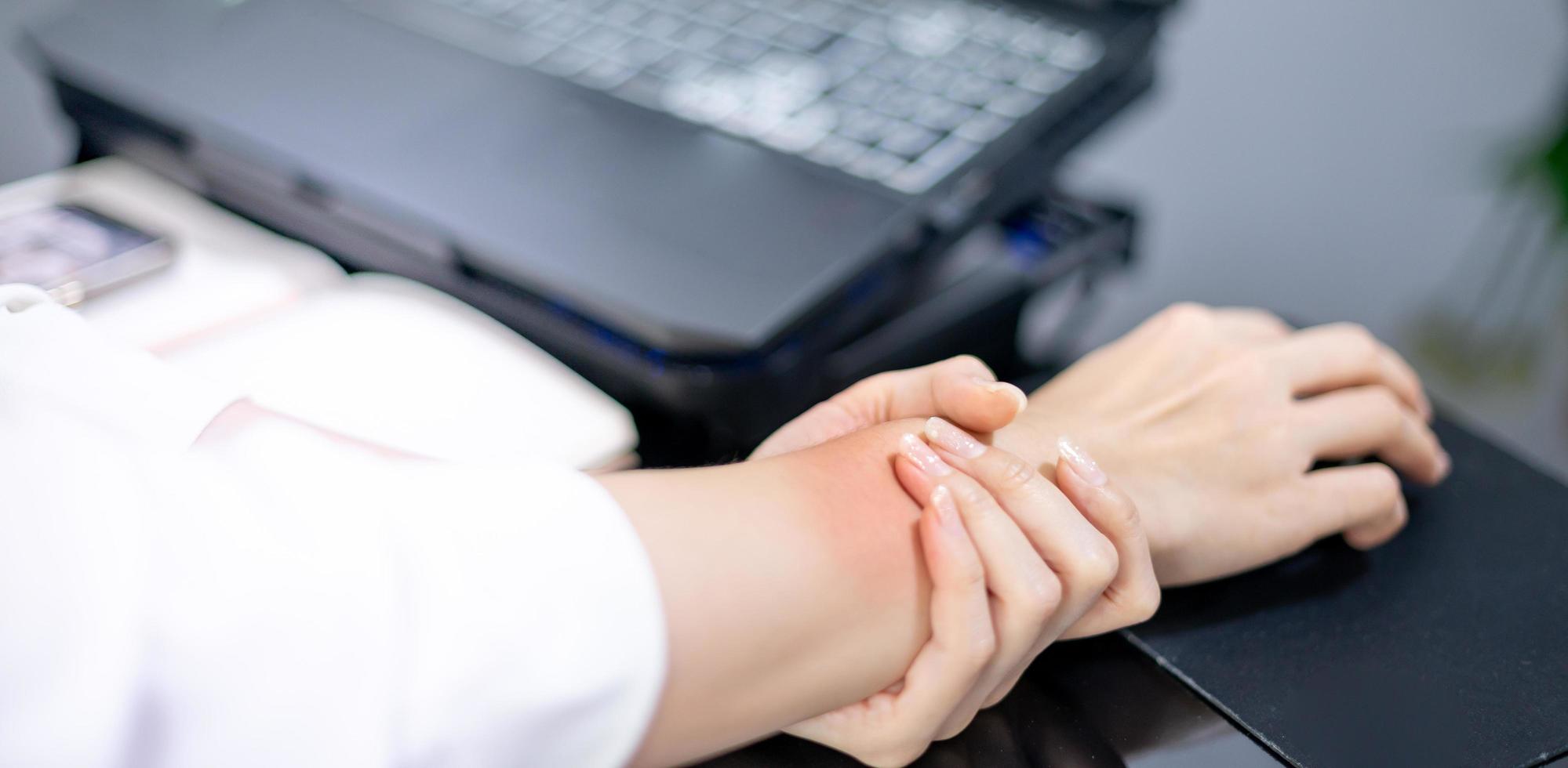 Asian woman holding her sore hand on wrist close-up. Pain from using computer. Office syndrome hand pain by working in front of the laptop. photo