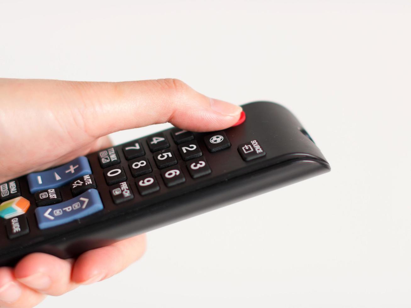 A hand holding and press at power button on television remote control on white background. photo