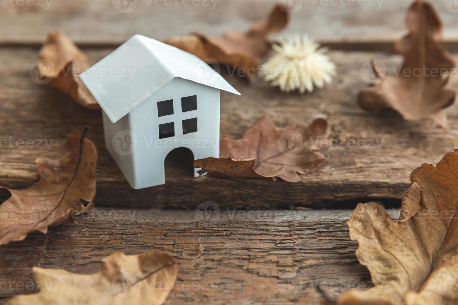 Autumnal Background. Toy house and dried fall leaves on wooden background. Thanksgiving banner copy space. Hygge mood cold weather concept. Hello Autumn with family. photo
