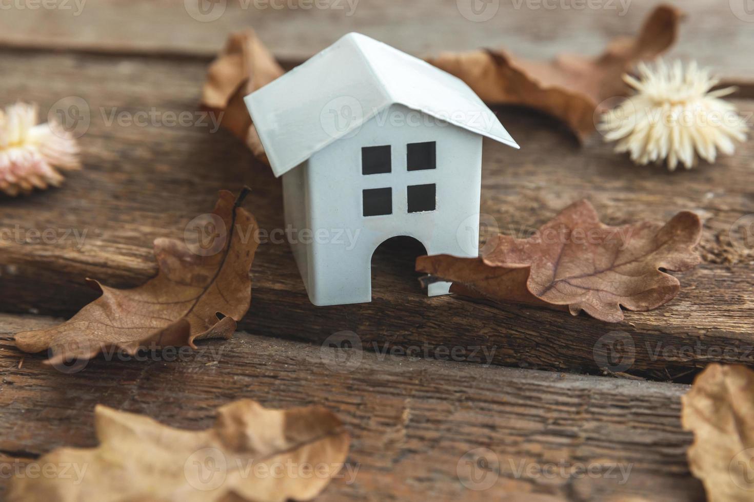 Autumnal Background. Toy house and dried fall leaves on wooden background. Thanksgiving banner copy space. Hygge mood cold weather concept. Hello Autumn with family. photo
