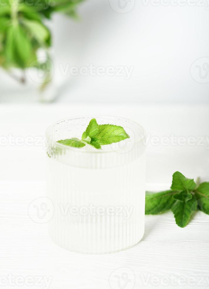glass of cold fresh detox water with mint leaves on white table, vertical. summer drinks, refreshing and cool non alcohol beverage. photo