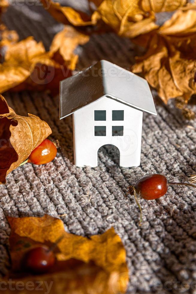 Autumnal Background. Toy house and dried orange fall maple leaves on grey knitted sweater. Thanksgiving banner copy space. Hygge mood cold weather concept. Hello Autumn with family photo