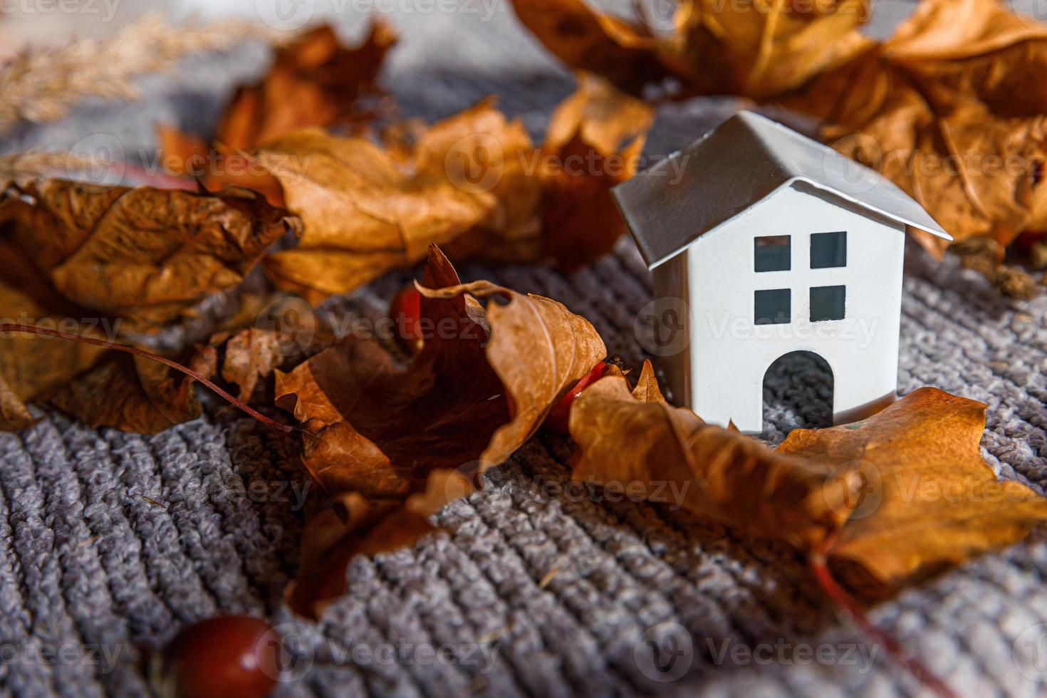 Autumnal Background. Toy house and dried orange fall maple leaves on grey knitted sweater. Thanksgiving banner copy space. Hygge mood cold weather concept. Hello Autumn with family photo