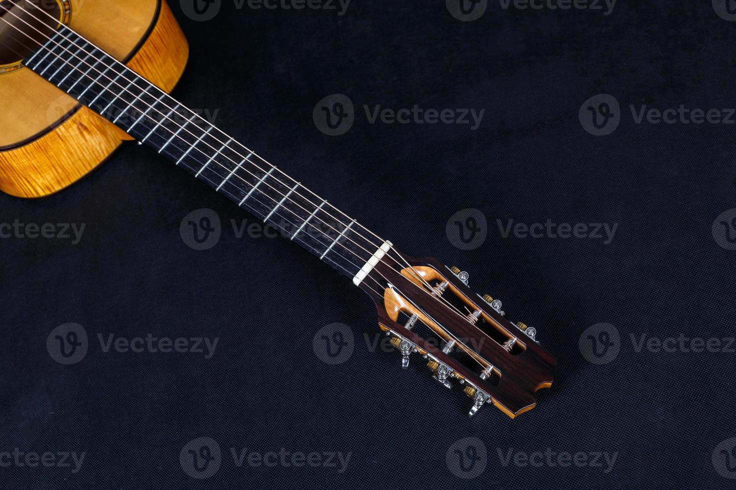 Tuning pegs on wooden machine head of six strings acoustic guitar neck on black background photo