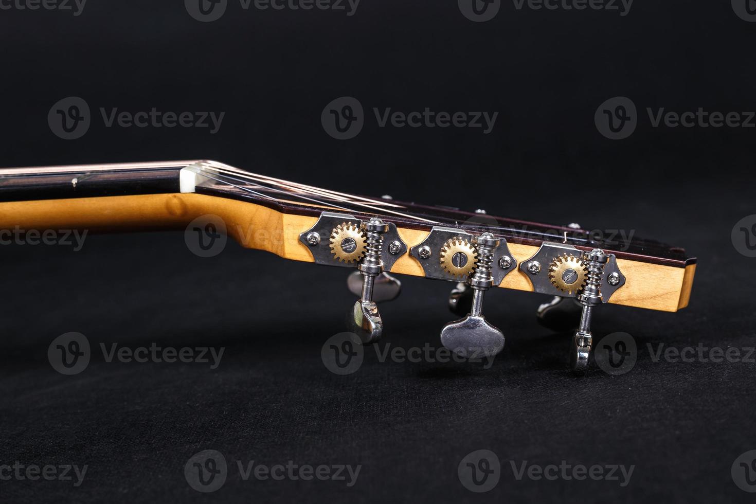 Tuning pegs on wooden machine head of six strings acoustic guitar neck on black background photo