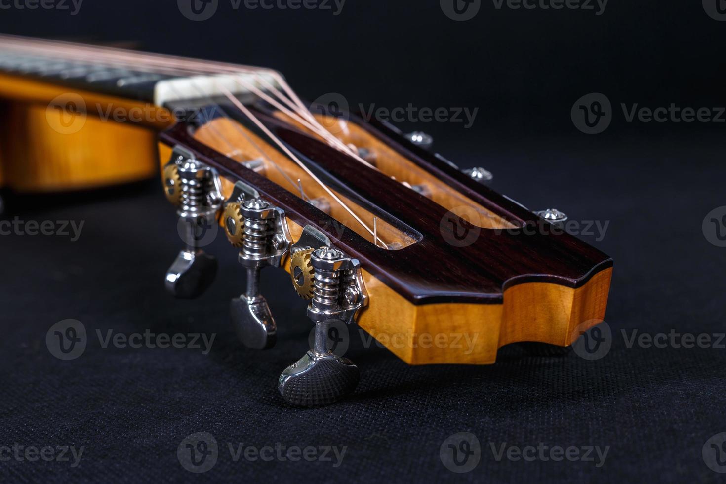 Tuning pegs on wooden machine head of six strings acoustic guitar neck on black background photo