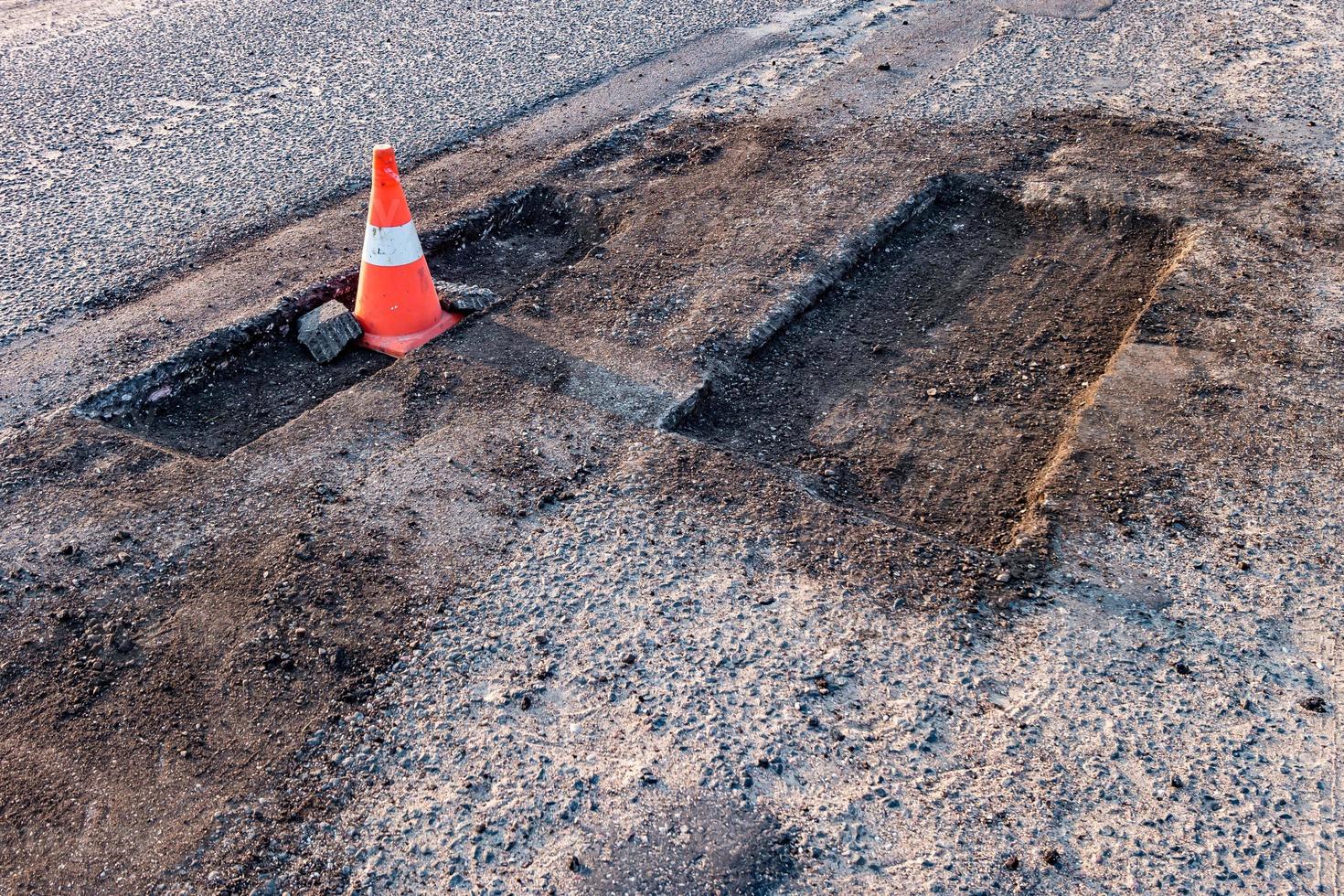 cono de peligro de tráfico naranja blanco en la reparación de carreteras de asfalto foto