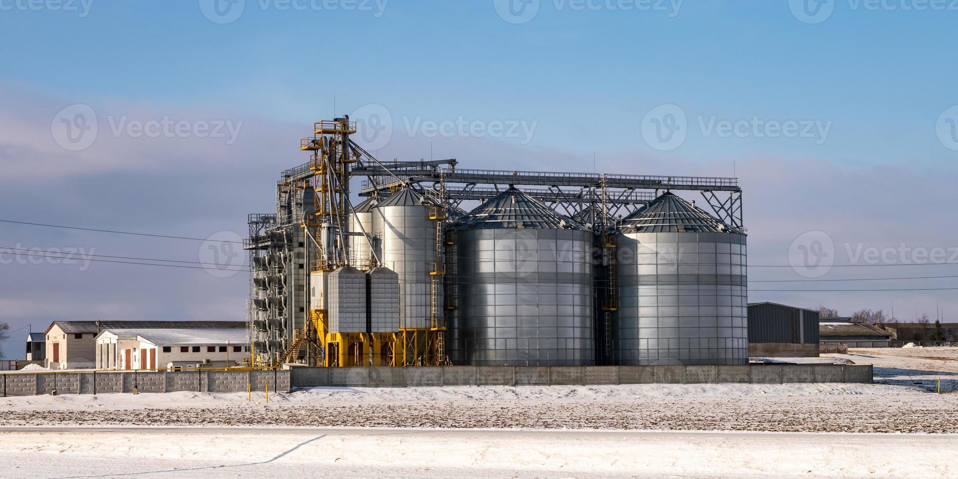 agro silos granary elevator in winter day in snowy field. Silos on agro-processing manufacturing plant for processing drying cleaning and storage of agricultural products, flour, cereals and grain. photo