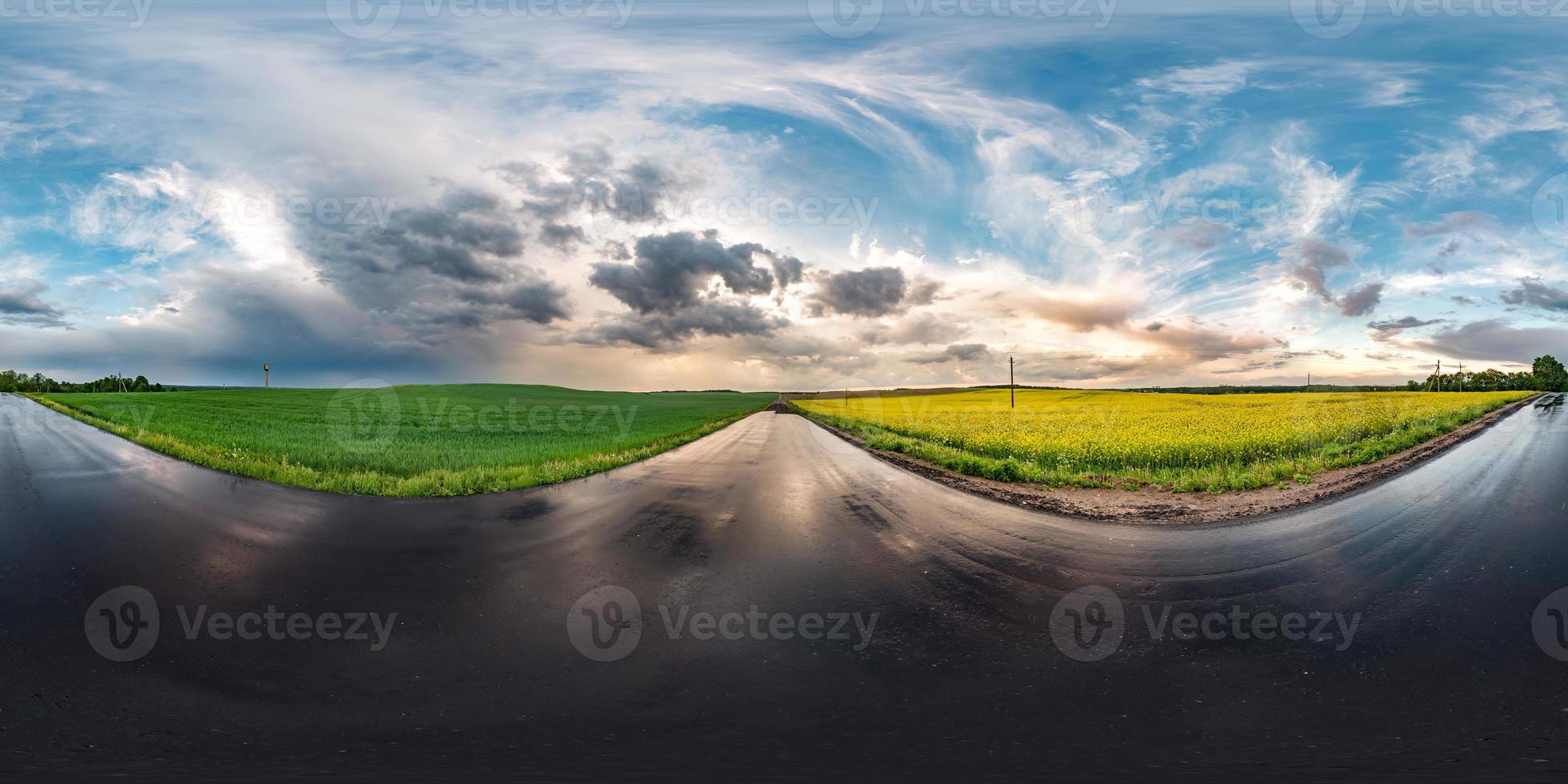 panorama hdri esférico completo sin costuras vista en ángulo de 360 grados en carretera asfaltada húmeda entre campos de canola en la puesta de sol después de la tormenta con nubes impresionantes en proyección equirectangular, contenido vr ar foto