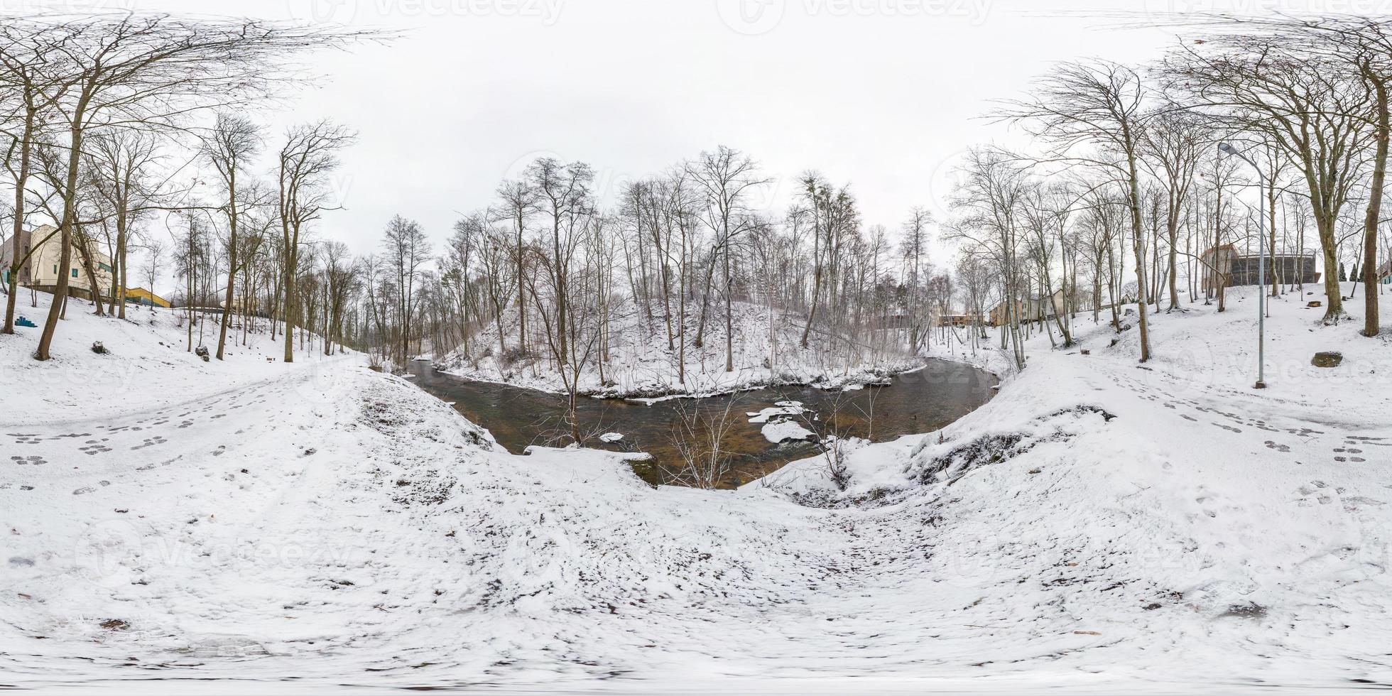 Winter full spherical seamless panorama 360 degrees angle view on road in a snowy park with gray pale sky near small river in equirectangular projection. VR AR content photo