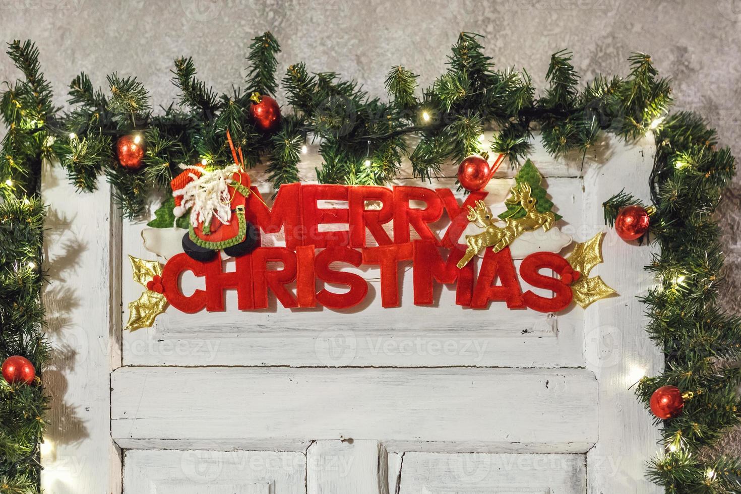 the inscription of a merry christmas on a white wooden door, surrounded by fir branches and toys photo