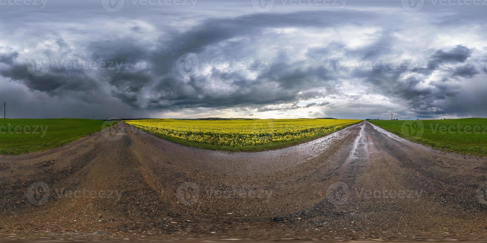 vista de ángulo de 360 grados de panorama hdri esférico completo en carretera asfaltada húmeda sin tráfico cerca de campos de canola de colza con cielo negro después de tormenta en proyección equirectangular, contenido vr ar foto