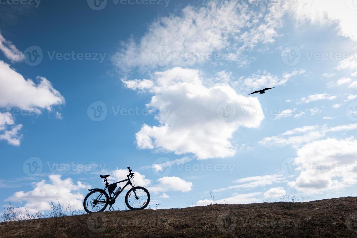 Bike silhouette in blue sky with clouds. symbol of independence and freedom with flying bird photo
