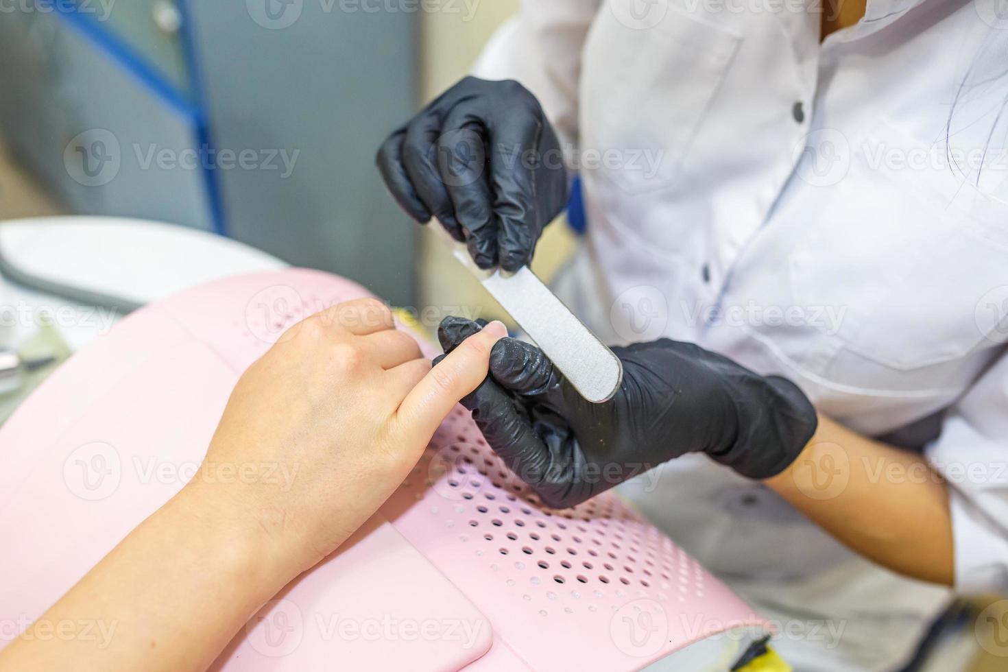 the master in black gloves in the salon makes manicure pedicure to the client photo