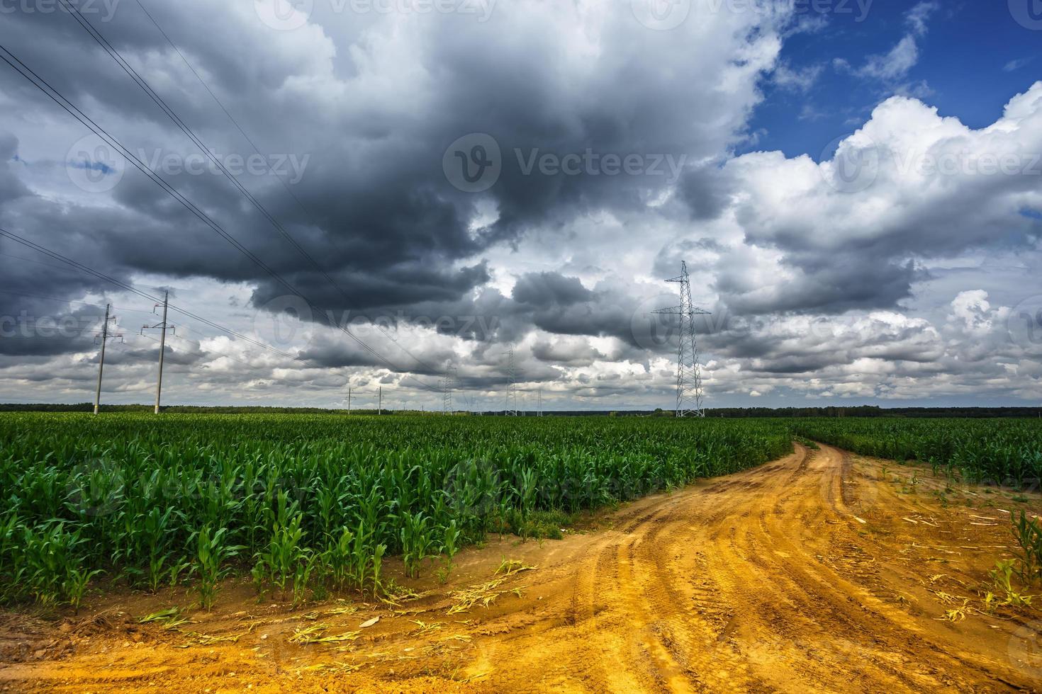 silueta de las torres de pilón eléctrico de alto voltaje en el fondo de hermosas nubes de tormenta cerca de la carretera de arena amarilla foto