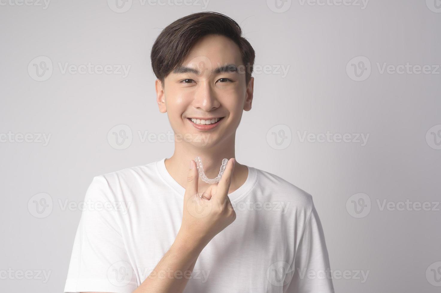 joven sonriente sosteniendo llaves invisalign sobre estudio de fondo blanco, cuidado de la salud dental y concepto de ortodoncia. foto