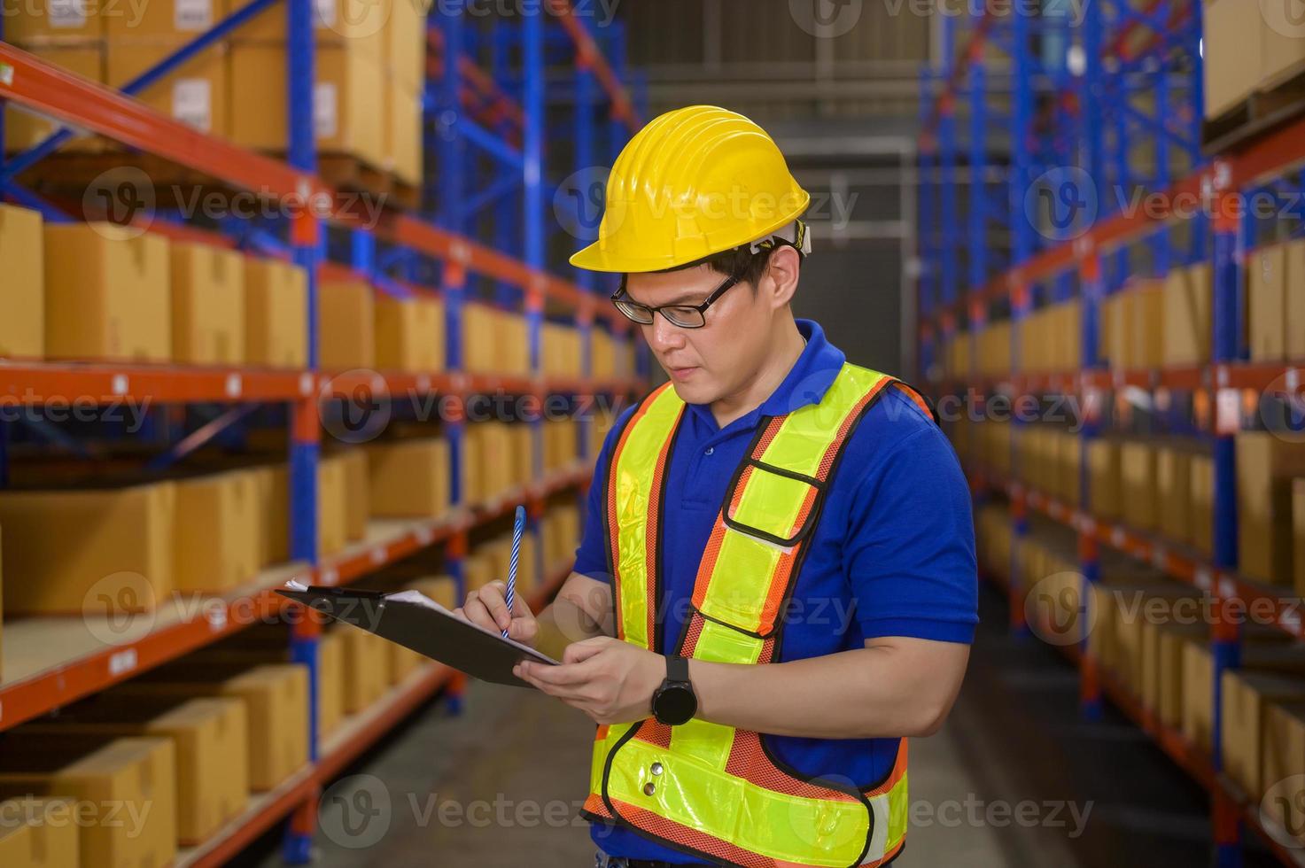 Young worker wearing helmet checking inventory and counting product on shelf in modern warehouse. photo