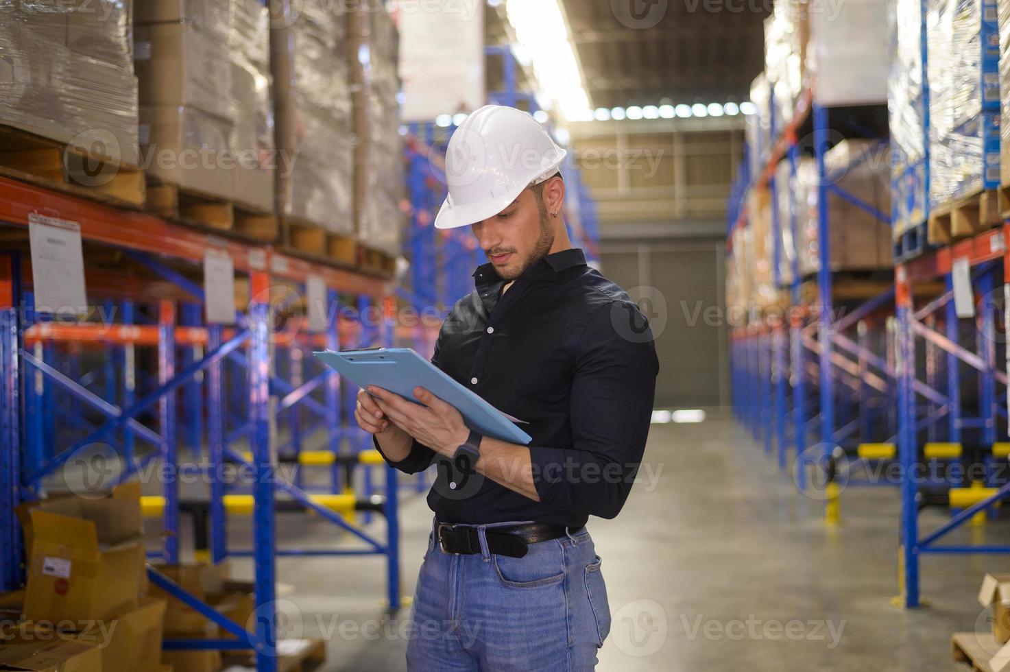 Young worker wearing helmet checking inventory and counting product on shelf in modern warehouse. photo