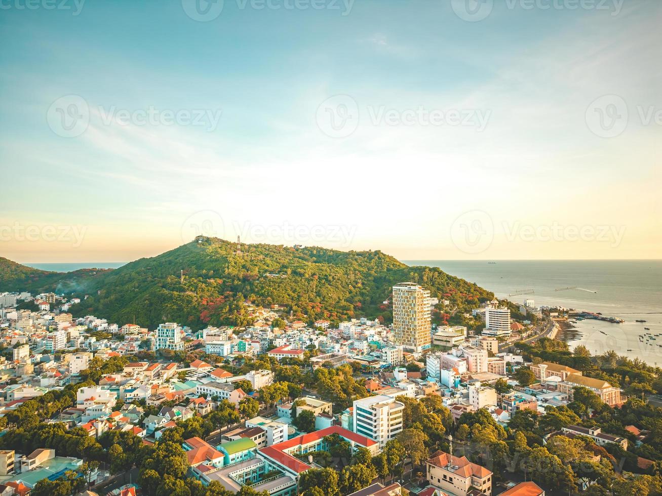 Vung Tau city aerial view with beautiful sunset and so many boats. Panoramic coastal Vung Tau view from above, with waves, coastline, streets, coconut trees and Tao Phung mountain in Vietnam. photo