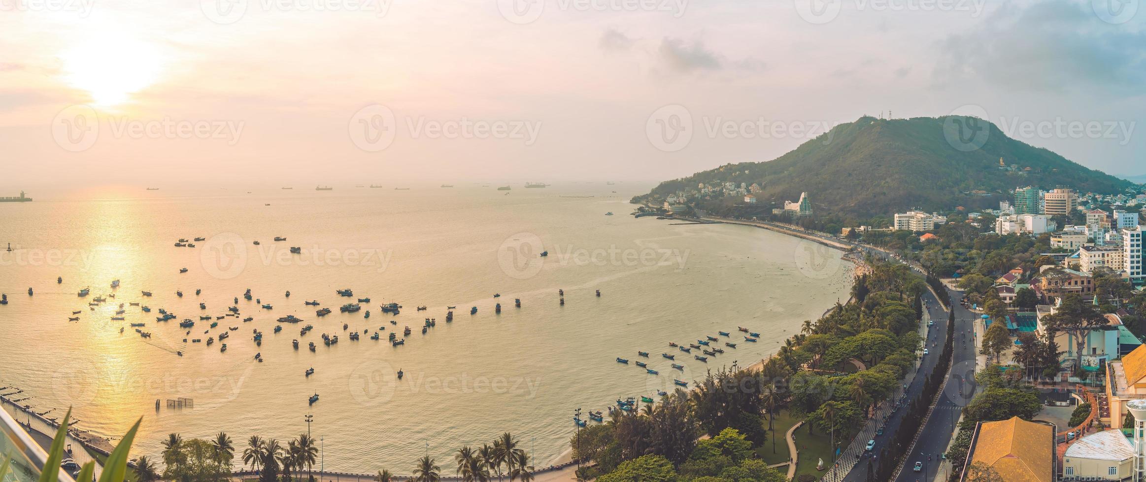 Vung Tau city aerial view with beautiful sunset and so many boats. Panoramic coastal Vung Tau view from above, with waves, coastline, streets, coconut trees and Tao Phung mountain in Vietnam. photo